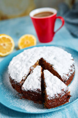 cut biscuit sprinkled with powdered sugar on the blue plate and red cup of coffee, cut lemon and badon on blue wooden background