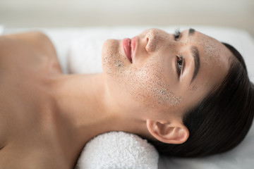 Peace and comfort. Close up of serene asian girl lying with scrub mask on her face at spa - Powered by Adobe