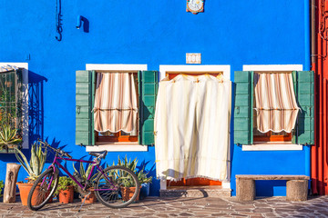 Beautiful blue house with a bicycle, plants and bench. Colorful houses in Burano island near Venice, Italy.