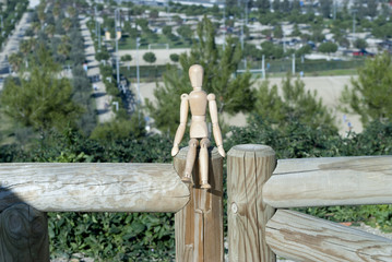 Wooden puppet sitting on wooden trunk where you can see down a park