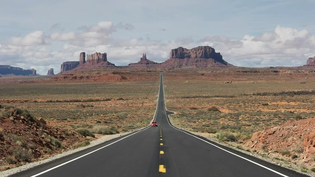 a red car drives towards the camera on hwy 163 at monument valley in utah, usa