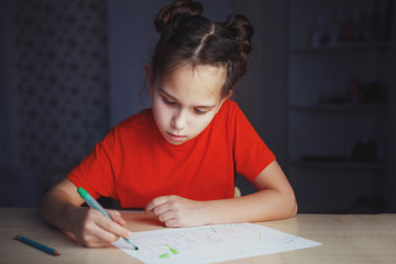 little girl draws a marker while sitting at the table at home