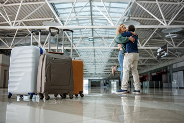 Fototapeta premium Low angle of happy man and woman hugging tight after a long separation. Focus on luggage