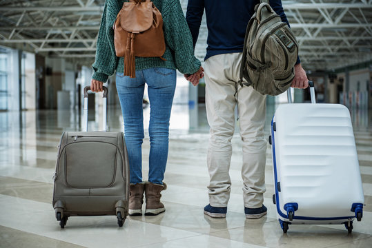 Man and woman holding each other hands while standing at the airport with big cases. Close up of their body