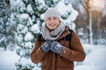 Fototapeta premium Waist up portrait of cheerful young man standing in winter forest and smiling. He is looking at camera with happiness