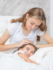 Young mom stroking her daughter on the bed