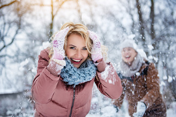 Waist up portrait of excited young woman covering her head from snow by hands. She is looking at...
