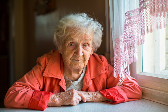 Portrait of an elderly woman sitting in the cloak at the table.