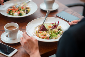 Close up big portion of salad locating on desk. Female eating it. Meal concept
