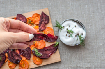 vegetable chips from carrots and beets with greens close-up and human hand in frame