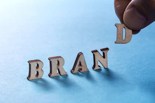 BRAMD from wooden letters on a blue background, a man's hand holds a letter D. Building a brand and bringing it to the market