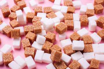 White and brown cane sugar cubes scattered on a pink background. Texture background