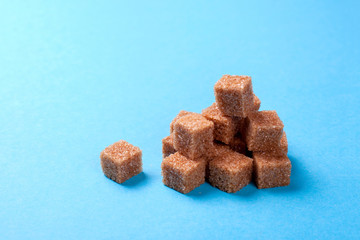 Brown cane sugar cubes heap on a blue background. Copy space for text