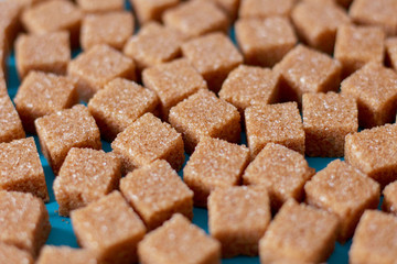 Brown cane sugar cubes scattered on a black background. Texture background