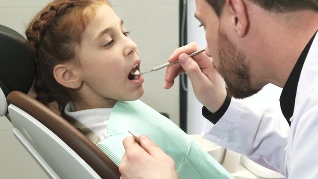 A professional doctor very carefully examines the teeth of a girl