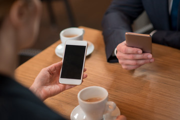 Close up female hand holding modern smartphone. She sitting at table opposite partner. Technology concept