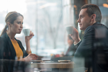 Smiling female talking with happy man while locating at desk in confectionary shop. Glad colleagues tasting cups of coffee. Break concept