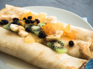 Delicious pancakes, decorated with pieces of banana, kiwi and orange, soaked in maple syrup
