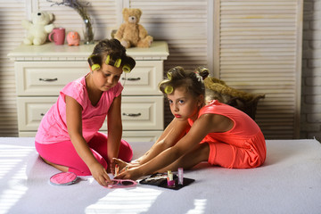 Little girls with curlers play with makeup in childroom