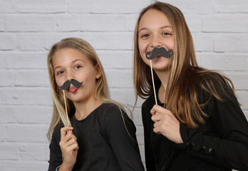 Portrait of two best friends sister girls having fun and posing with fake mustache on a stick....