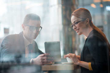 Portrait of outgoing male and happy businesswoman looking at electronic tablet. Cheerful colleagues sitting at desk. Comrades indoor. Job concept