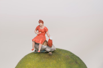 Miniatur Figur einer Frau in rotem Kleid auf einem Stein sitzend