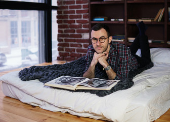 Young bearded man with glasses lying on bed and smiling