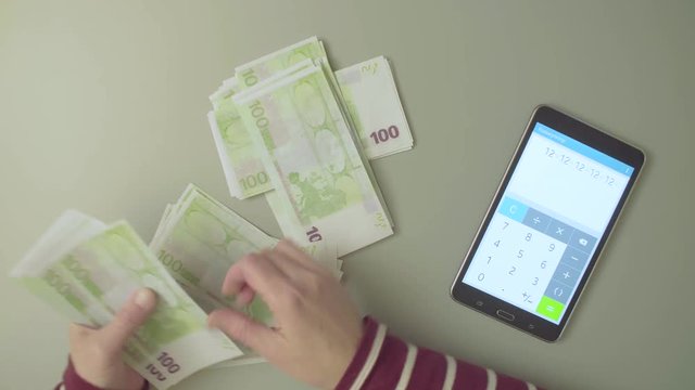 Top view. Female hands counts money and summarize the result on the calculator. Text on the tablet - calculator