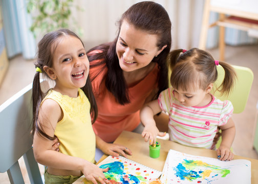 Mother and daughters are painting together. Happy family are coloring with paintbrush. Woman and children have a fun pastime.