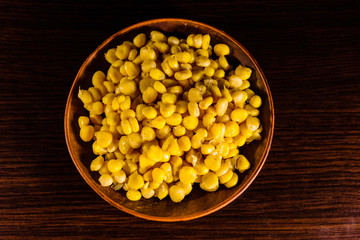 Ceramic plate with canned corn seeds on wooden table. Top view