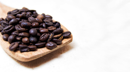 close up of roasted coffee beans on a wood spoon with white background with space for text.