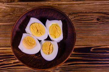 Ceramic plate with peeled boiled eggs on wooden table. Top view