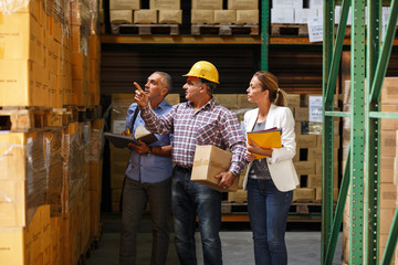 Fototapeta premium Two customs managers and warehouse worker checking list and inventory on the shelf in storehouse.