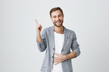 Good-looking happy positive shocked bearded European male dressed in trendy jacket pointing his...
