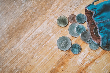 Thai and Hong Kong coins in blue fabric bag on wood table.