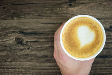 A man holding latte coffee with art heart milk isolated on brown wood table background. Flat lay with a cup of coffee valentine concept.