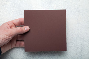 Obraz premium Male hands holding brown Square Flyer / Invitation Mock-Up.