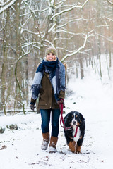 Fototapeta na wymiar Frau mit ihrem Hund wandert oder geht spazieren im Winter auf einem Weg, der mit Schnee bedeckt ist