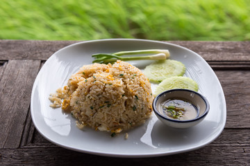Crab meat fried rice with vegetables in dish on wooden table near rice field