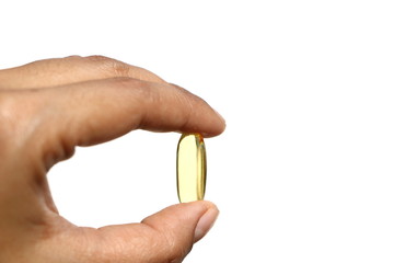 Woman hand holding single yellow Cod Liver Oil capsule on white background, fish oil is a dietary supplement derived from liver of cod fish, have omega-3 fatty acids, EPA, DHA, vitamin A and D