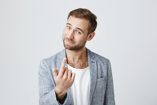 Handsome man with dark hair, stylish haircut, blue eyes, and beard looks with appeal at camera, isolated against gray background. Confident european gestures like says come here. Body language