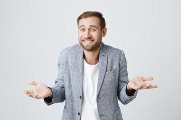 Clueless puzzled attractive man with beard, smiling broadly, having hesitation shrugging shoulders...