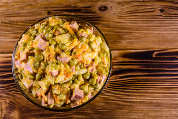 Salad with sausage, green pea, onion and carrot in glass bowl on wooden table. Top view