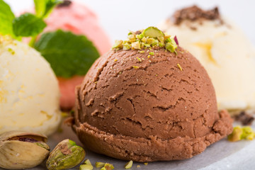 Assorted ice cream scoops of different colors and flavours in white bowl with pistachio nuts, chocolate and mint decoration. Summer food concept.