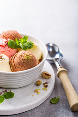 Set of ice cream scoops of different colors and flavours in white bowl with pistachio nuts and mint decoration. Summer food concept with copy space.