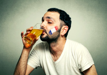 Funny sport fan with flag painted on face drinking beer