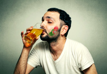 Funny sport fan with flag painted on face drinking beer