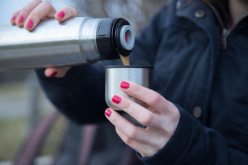 Junge Frau mit roten Fingernägeln hält Kafee (Thermobecher) in der Hand