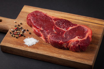 Beef steak on the wood black background. Horizontal photo. Food background. Marble the meat with pepper and salt on a dark background