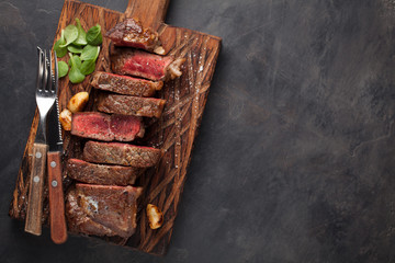 Closeup ready to eat steak new York beef breeds of black Angus with herbs, garlic and butter on a wooden Board. The finished dish for dinner on a dark stone background. Top view with copy space